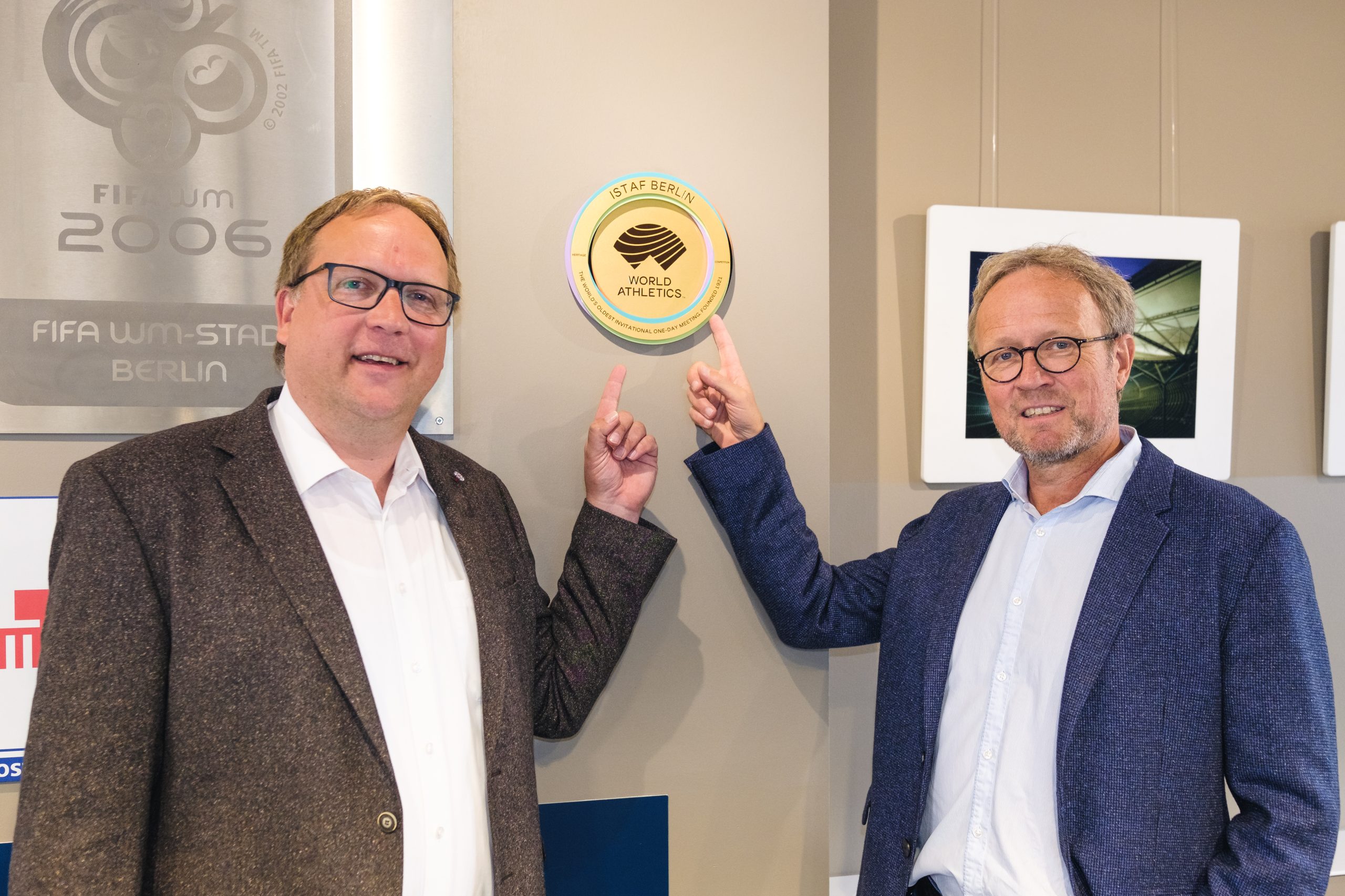 Timo Rohwedder, Geschäftsführer der Olympiastadion Berlin GmbH und Martin Seeber, Geschäftsführer von TOP Sportmarketing Berlin, zeigen im Olympiastadion Berlin Besucherzentrum auf die Plakette des ISTAF